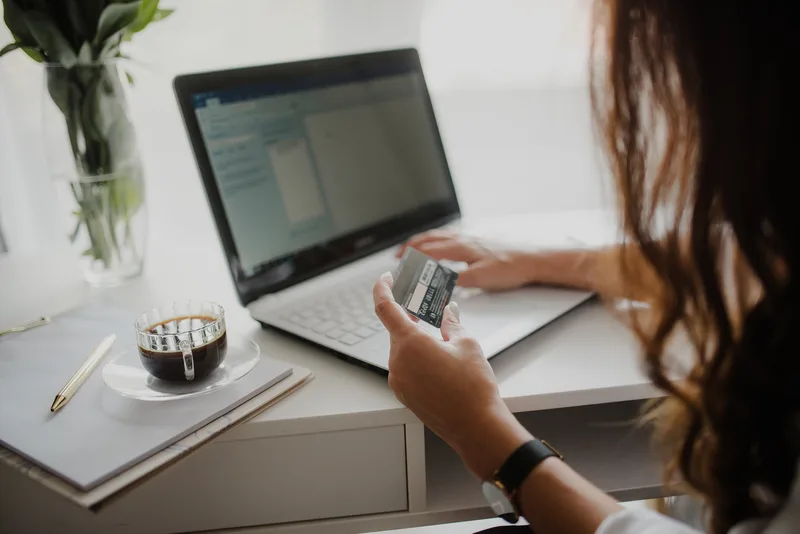 Woman looking closely at a credit card while working on her laptop