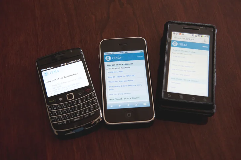 Three older smartphones on a wooden table each showing a mobile web page