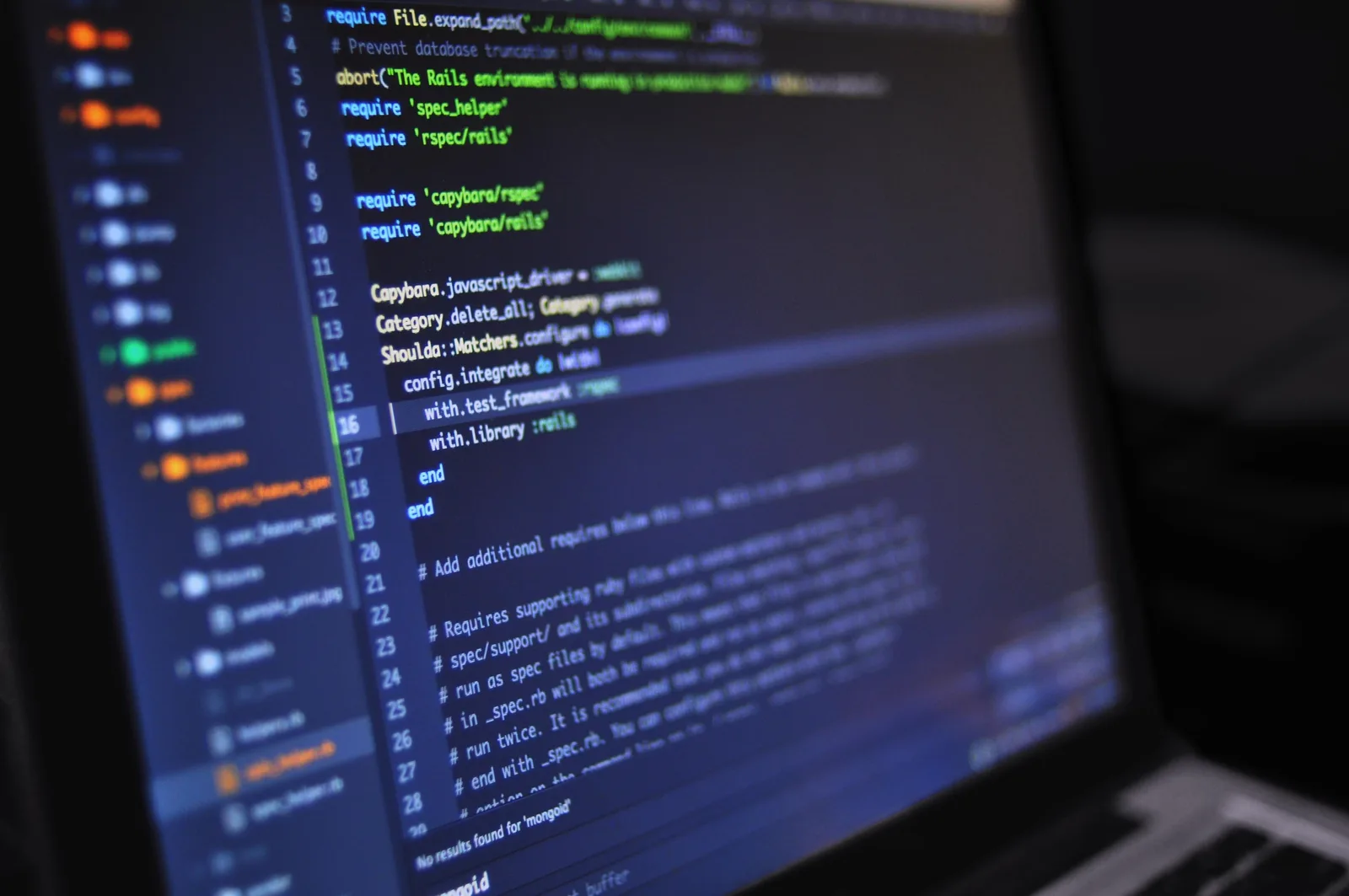 Laptop screen showing colourful source code in a dark code editor on a desk