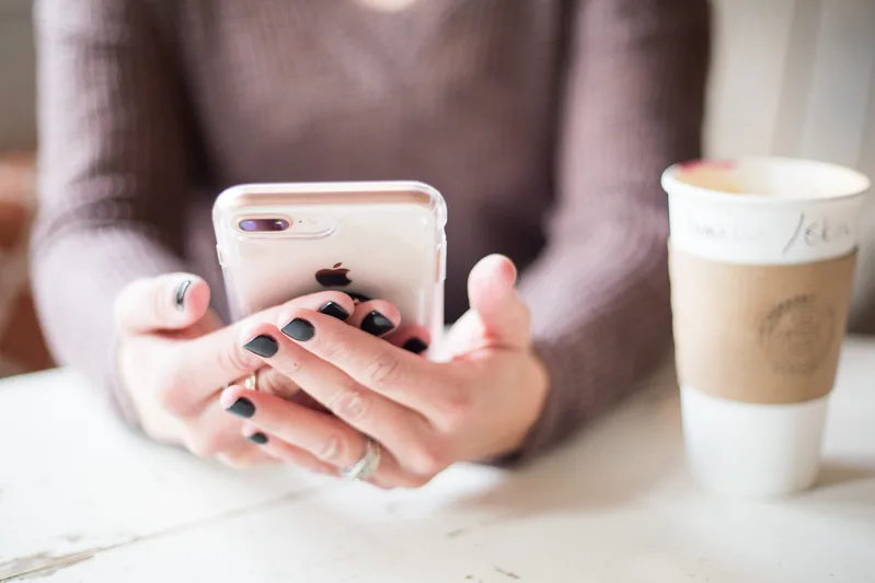Woman holding an iPhone and scrolling on its screen while sitting indoors