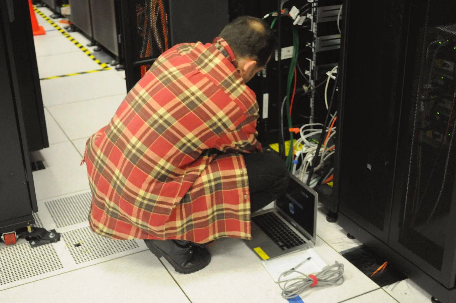 Technician using a laptop while working on cables at an open server rack
