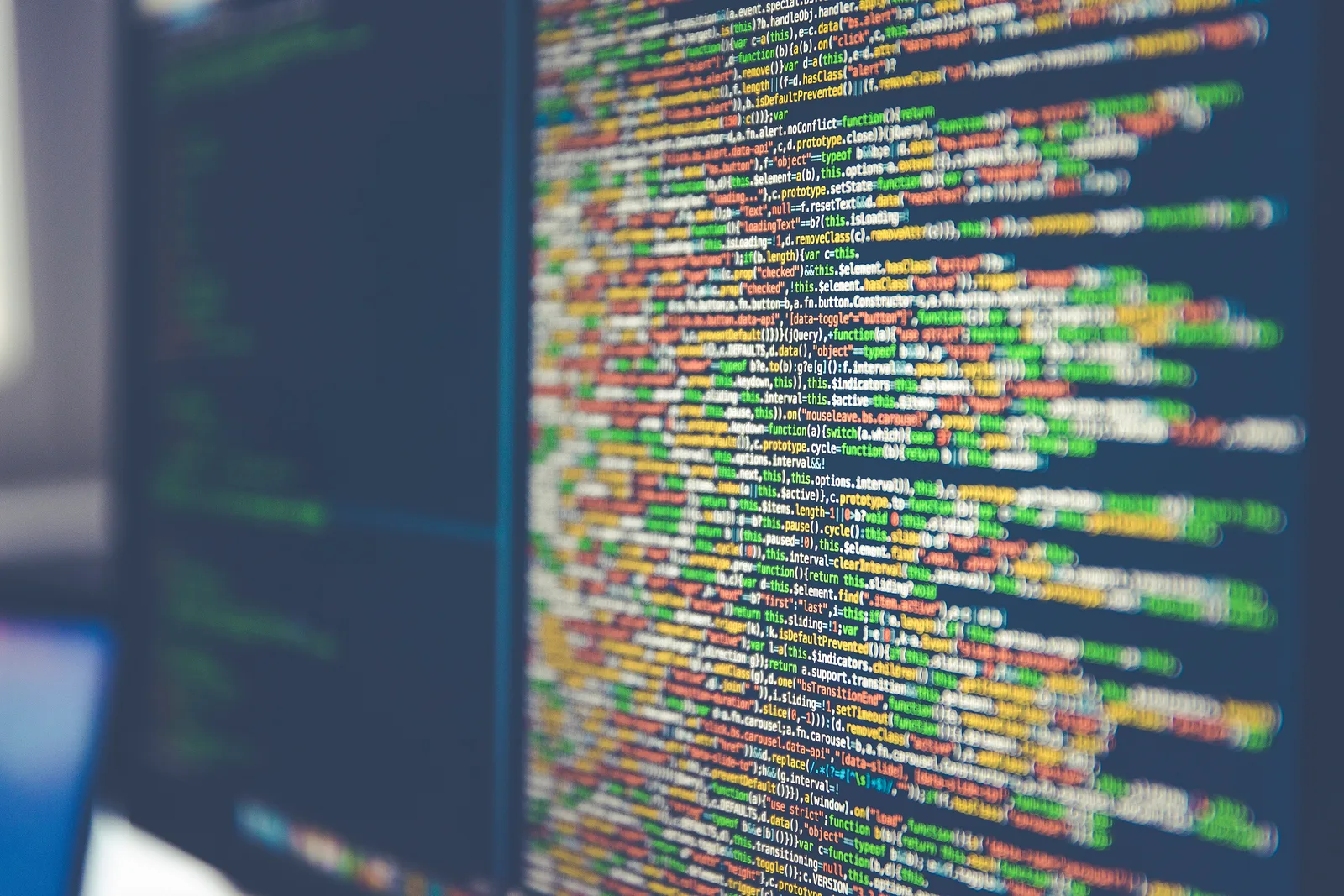 Dense lines of colourful syntax-highlighted code on a computer monitor, shot at an angle