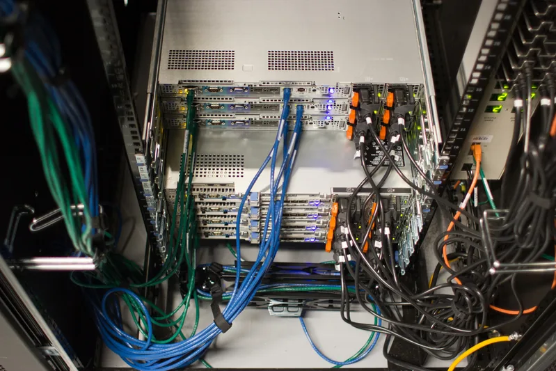 Back of a server rack with bundles of blue, green and orange network cables connected to equipment