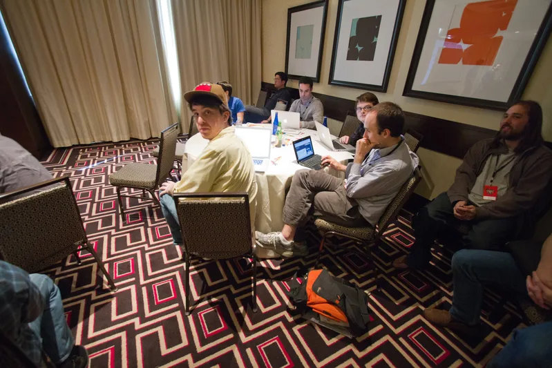 Conference attendees at a round table with open laptops during a JavaScript event
