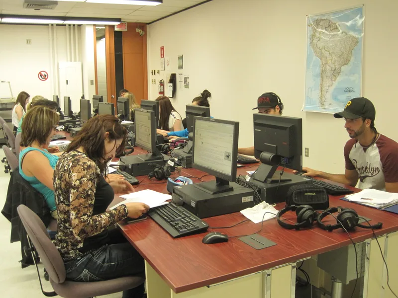 College students working at desktop computers with headphones in a classroom with a wall map