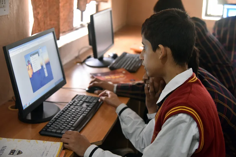 A school student in a red sweater using a desktop computer in a school computer lab
