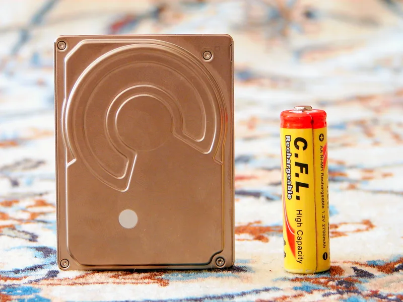Small failed laptop hard disk drive placed next to an AA battery for scale