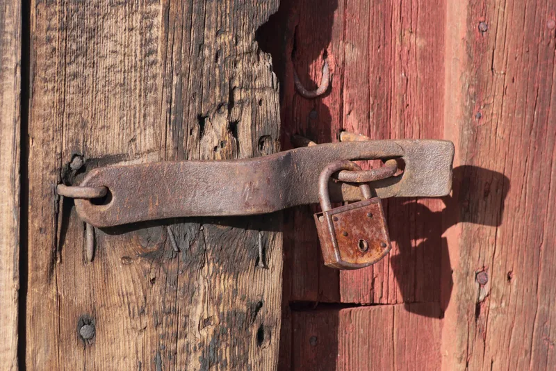 Rusty padlock securing a metal hasp on a weathered red wooden door
