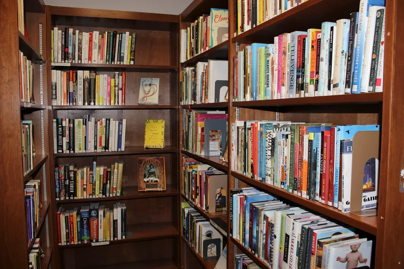 Corner of a small library with tall wooden shelves full of paperback and hardback books