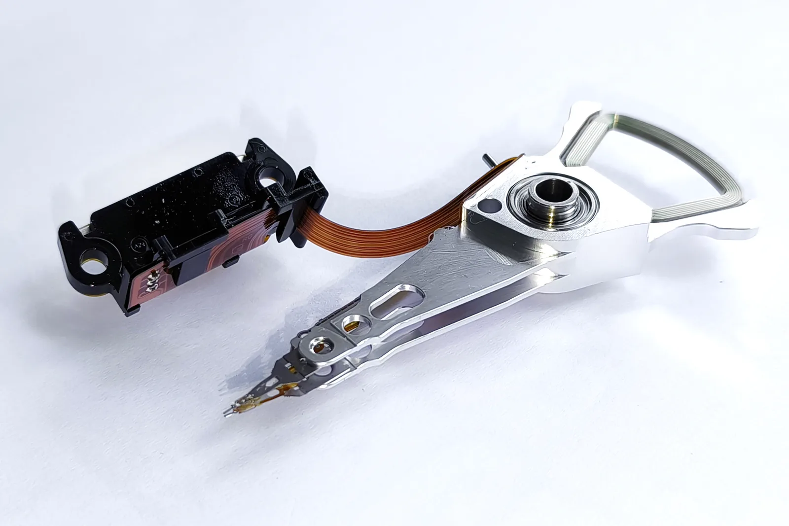 Hard disk drive actuator arm with its read head and ribbon cable, removed from the drive and photographed on white