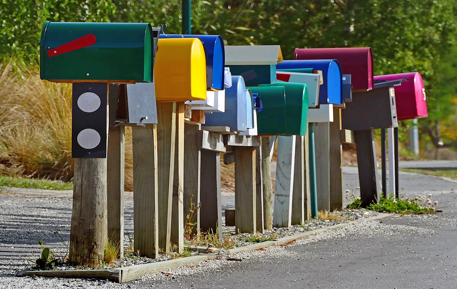 Row of colourful roadside mailboxes on wooden posts beside a country road