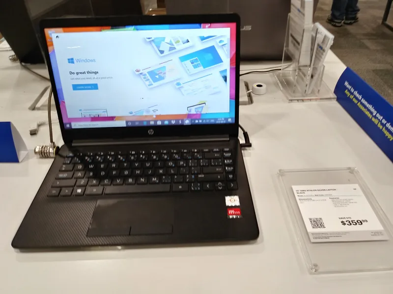 Black HP laptop on a shop display table showing the Windows 10 desktop, secured with a cable lock