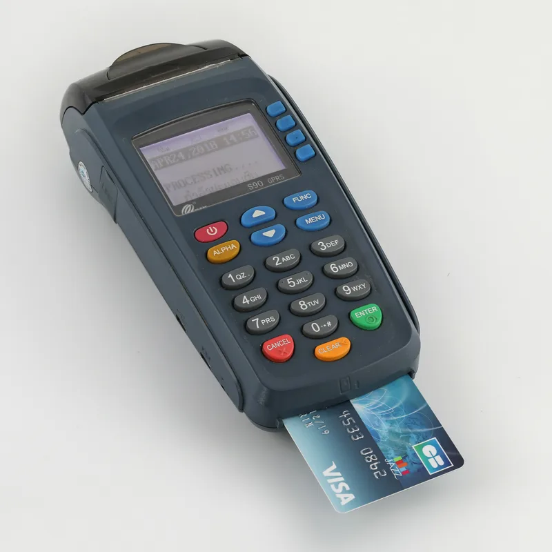 Handheld card payment terminal with a keypad and a bank card inserted, its screen showing Processing