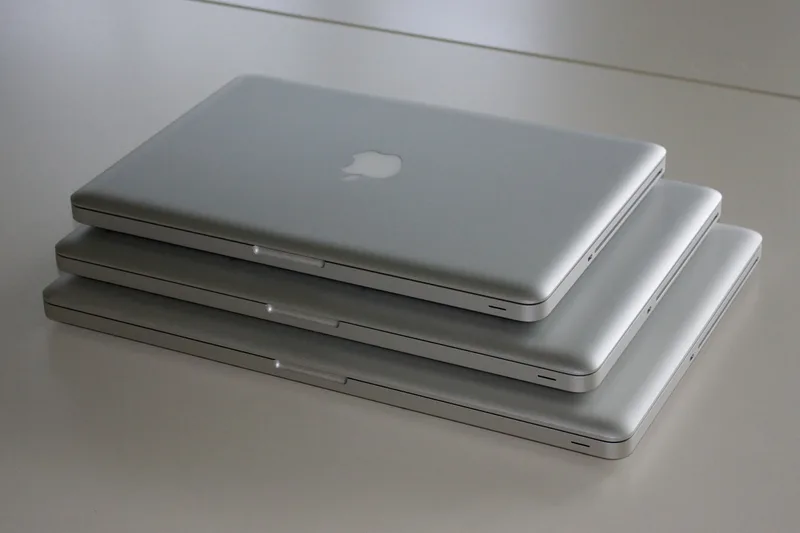 Three silver laptops of different sizes stacked on top of each other on a white table