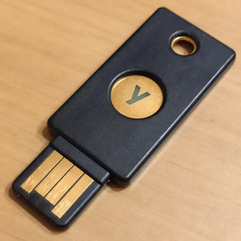 Black USB hardware security key with a gold touch contact lying on a wooden desk