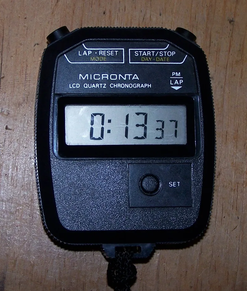 Black digital stopwatch on a wooden surface showing 0:13 37