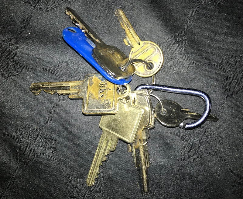 A bunch of different door keys on several key rings lying on a dark cloth