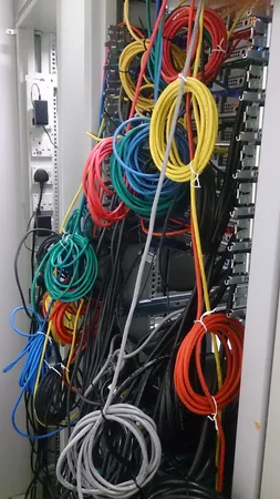 Coils of red, yellow, green, blue and grey network cables hanging in front of a server rack