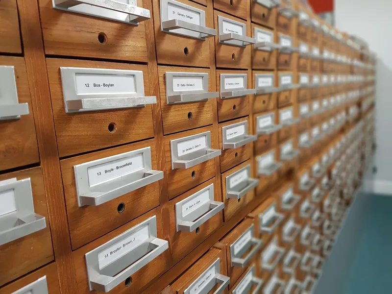 Long wooden card filing cabinet with rows of labelled drawers marked with alphabetical name ranges