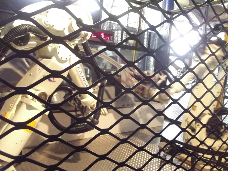 Industrial robotic arms on a car assembly line seen through a black metal safety mesh