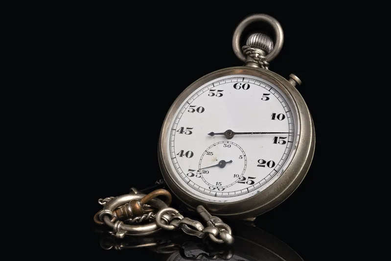 Vintage silver stopwatch with a white dial and chain against a black background