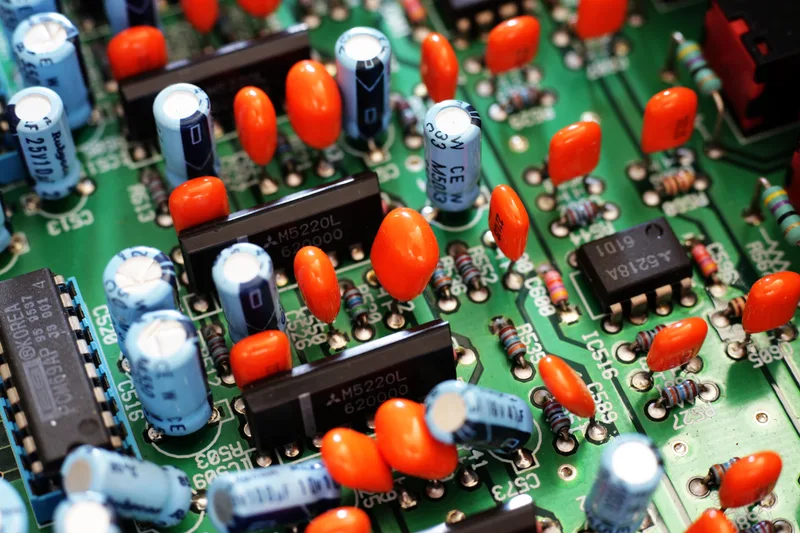 Close-up of a green circuit board crowded with orange capacitors, blue electrolytic capacitors and chips