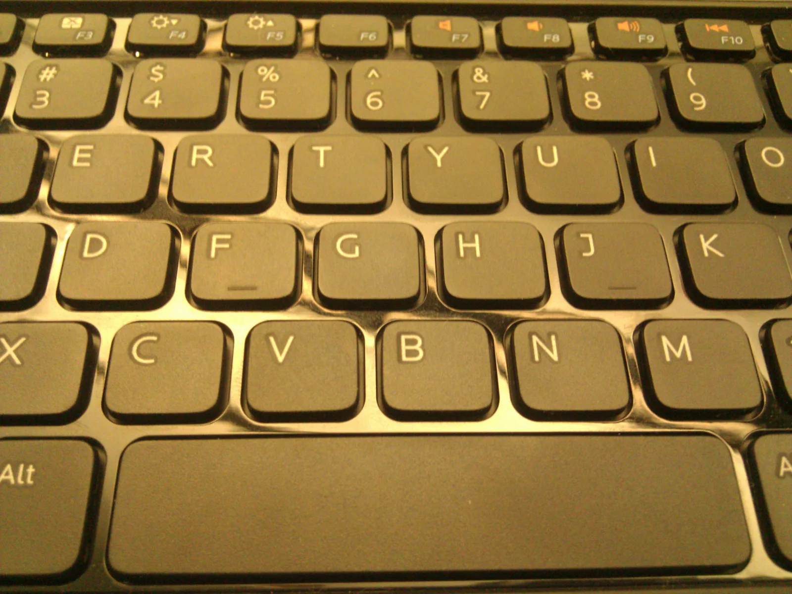 Close-up of a black laptop keyboard showing letter keys and the space bar under warm light
