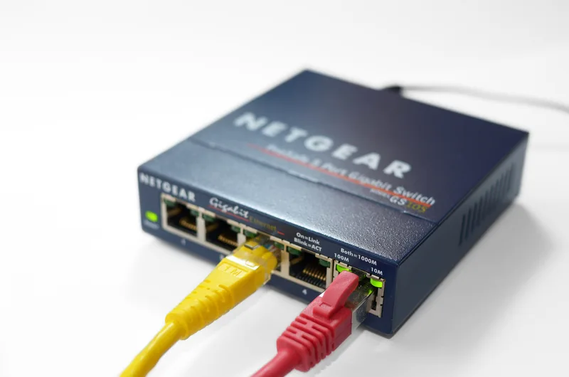 Small five-port Netgear gigabit Ethernet switch with a yellow and a red network cable plugged in and a green link light lit