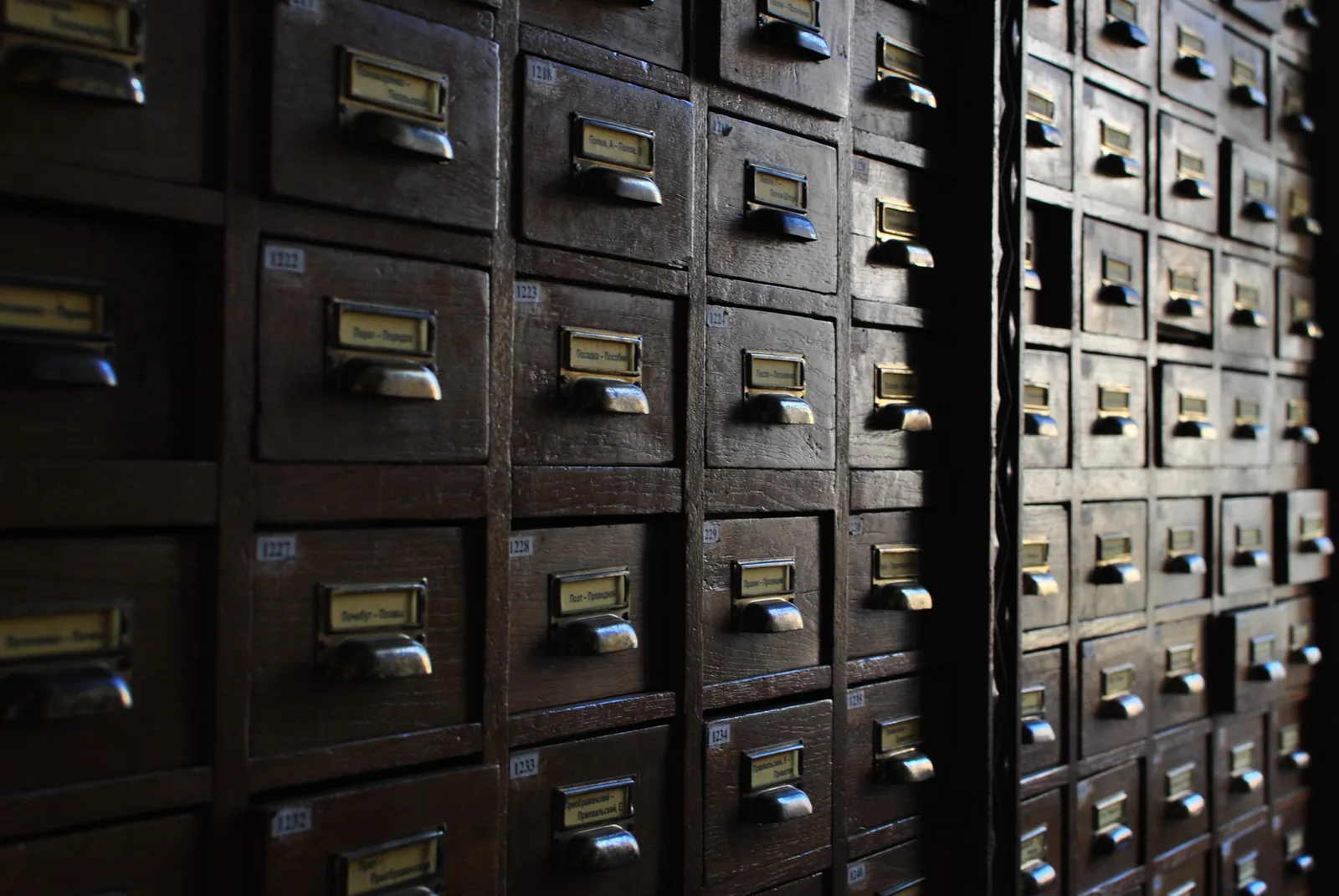 Rows of dark wooden card catalogue drawers with brass label holders and handles