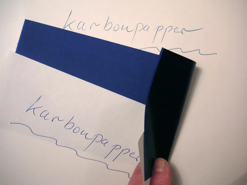 Sheet of blue carbon paper lifted from a page to reveal the handwritten word karbonpapper copied beneath