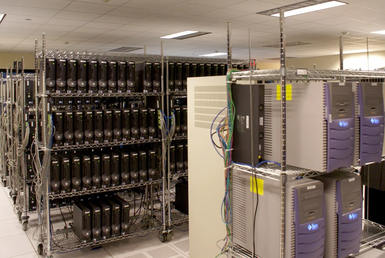 Server room with metal shelving full of tower servers and a rack of beige machines with blue lights