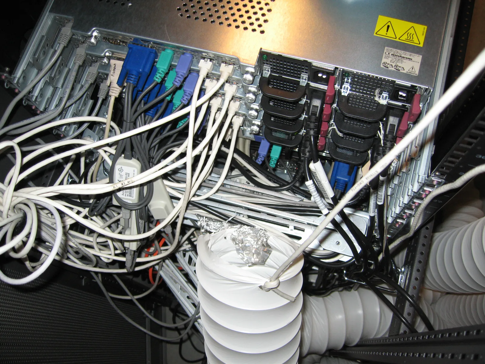 Open server rack with dense bundles of network and power cables and white air conditioning ducts