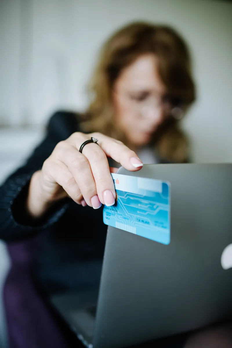 A woman holding a blue credit card while using a laptop to pay for an online order