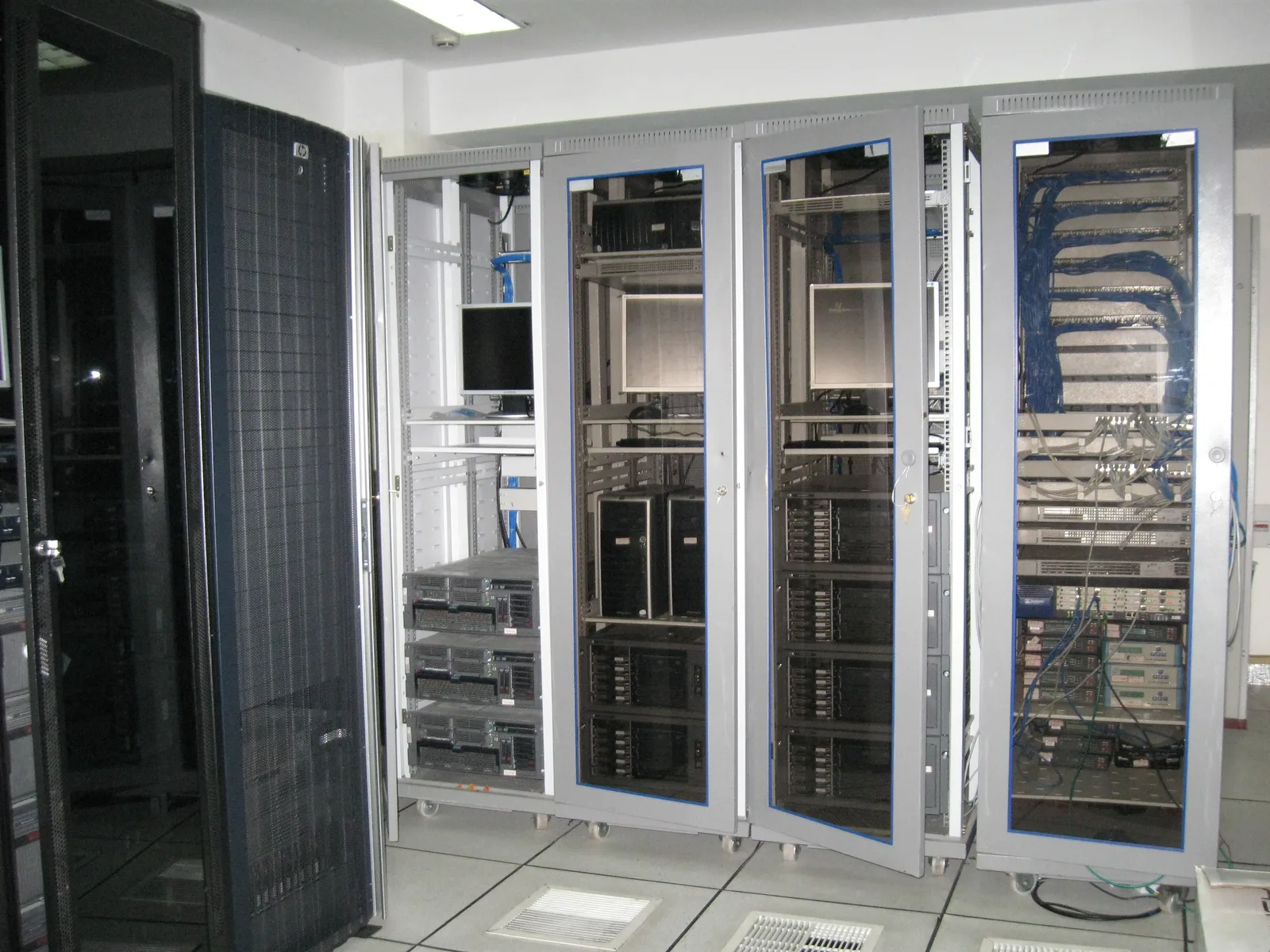 Row of grey server cabinets with glass doors holding rack servers in a white-tiled server room