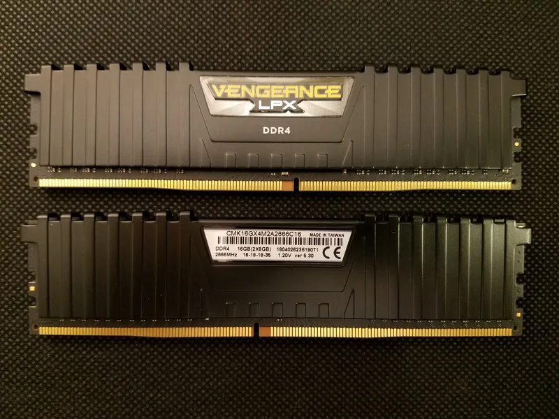 Two black Corsair Vengeance LPX DDR4 memory modules lying side by side on a dark textured surface