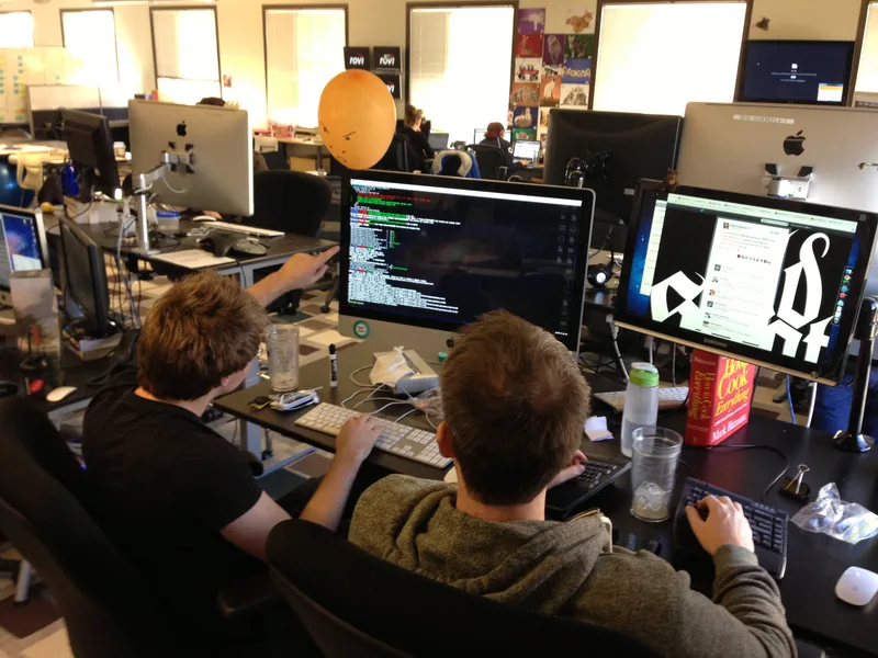Two engineers sitting side by side at desks with large monitors, one showing a terminal