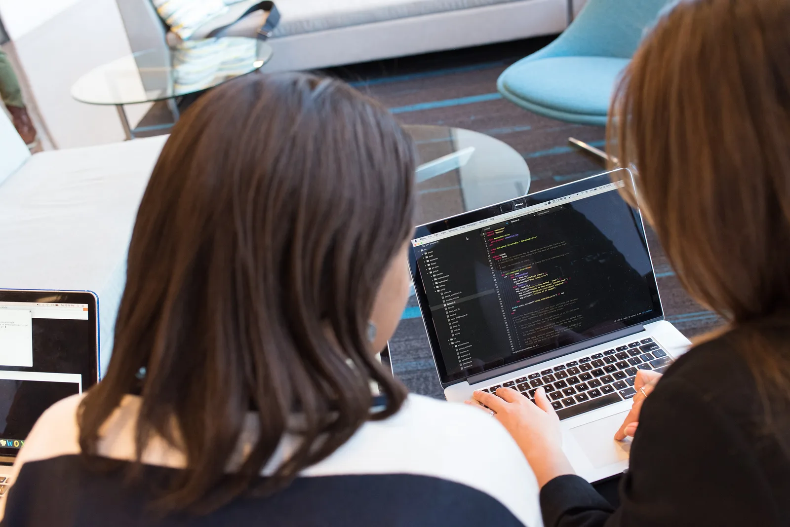 Two women looking at a laptop screen showing code in a dark-themed editor