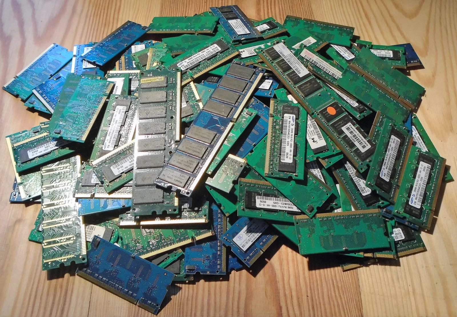 A large pile of green and blue laptop and desktop memory modules on a wooden table