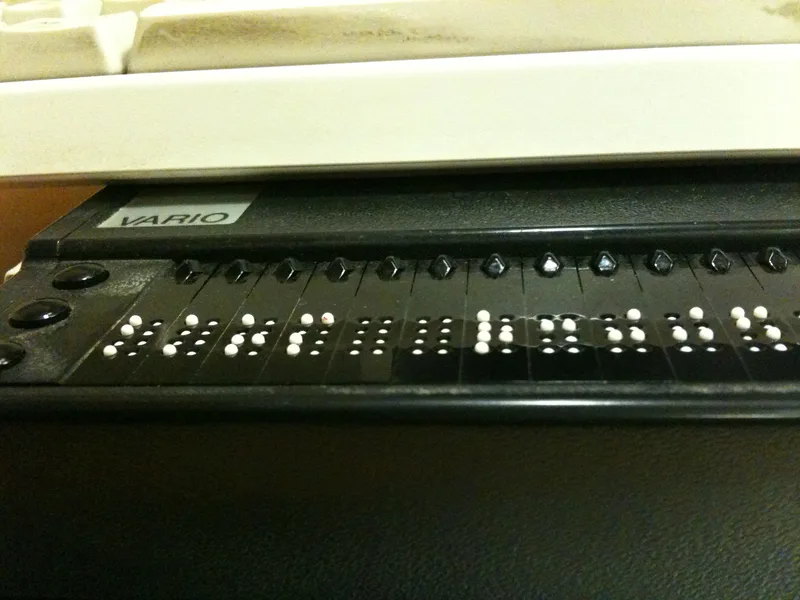 Close-up of a refreshable braille display in front of a computer keyboard, with raised white pins forming braille characters