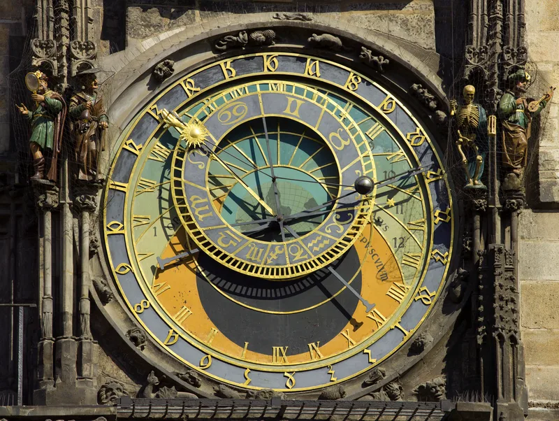 The ornate face of the Prague astronomical clock, with Roman numerals, a golden sun hand and zodiac ring, flanked by carved figures