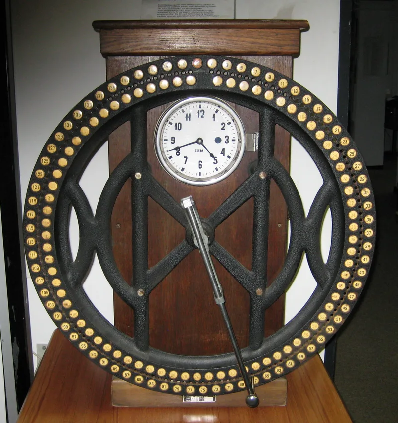 An early twentieth-century dial time recorder with a clock face, a large ring of numbered holes and a pointer arm, on a wooden cabinet