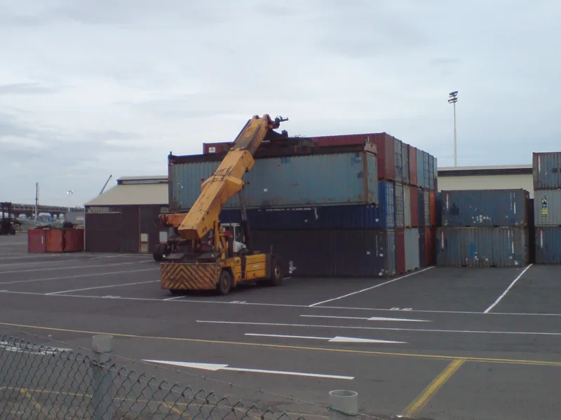 Yellow reach stacker lifting a shipping container onto a stack in an empty port yard