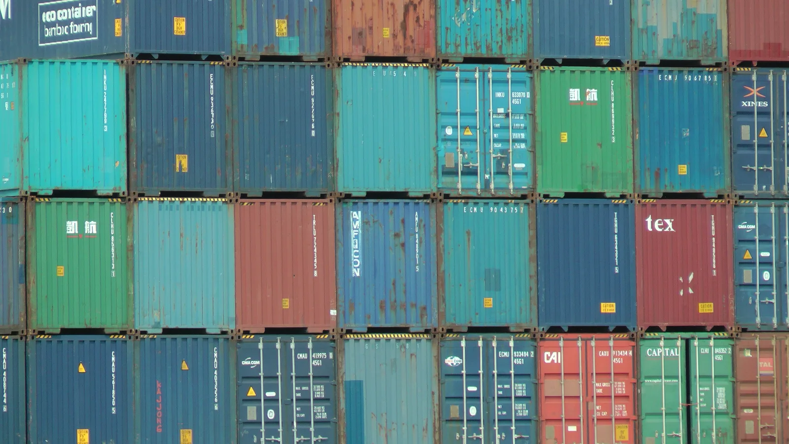 Wall of stacked shipping containers in blue, green, red and teal at the Port of Rotterdam