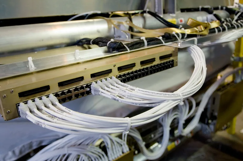 Patch panel with rows of white Ethernet cables bundled and routed into network equipment