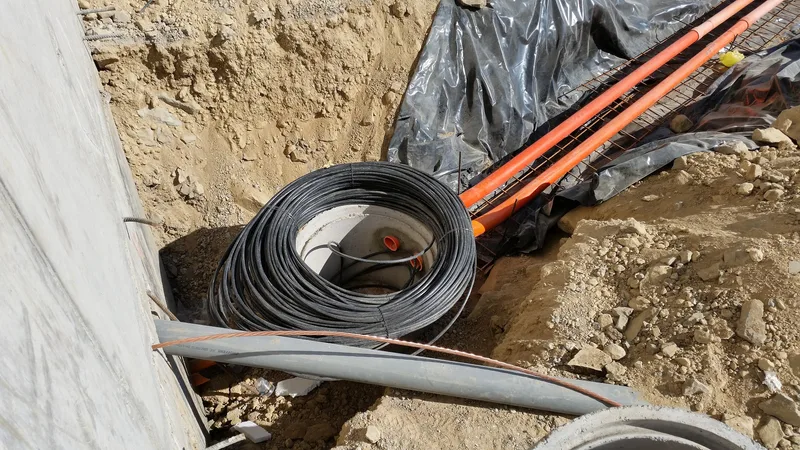 Coil of black fibre optic cable and orange ducts being laid in an excavated trench