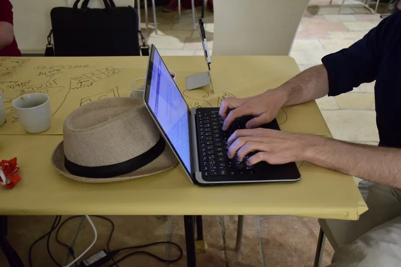 Developer typing on a laptop at a table covered with hand-drawn notes, next to a hat and a coffee cup