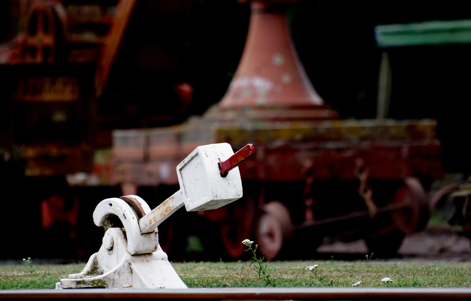 White-painted manual points lever with a red handle beside a railway track, old rolling stock blurred behind