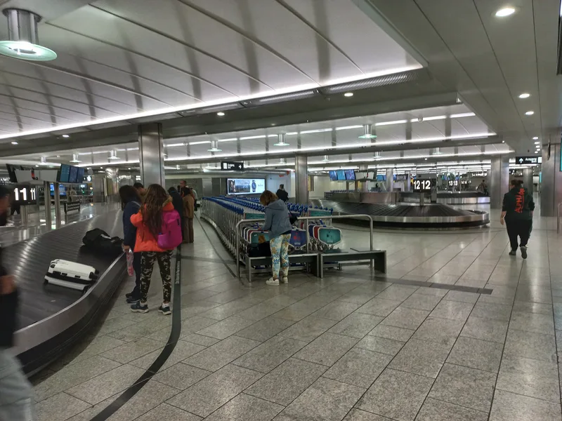 Travellers collecting suitcases from a baggage belt in the arrivals hall at Zurich Airport