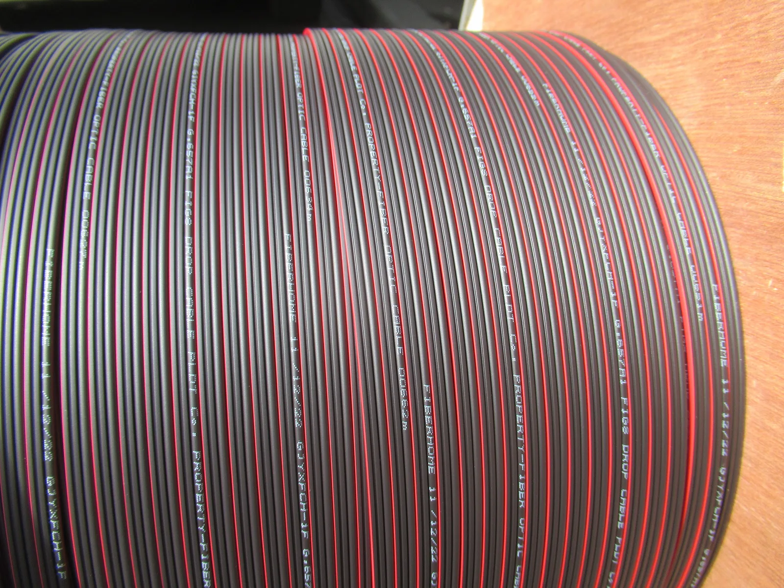 Close-up of a reel of black fibre-optic drop cables with red stripes and printed markings