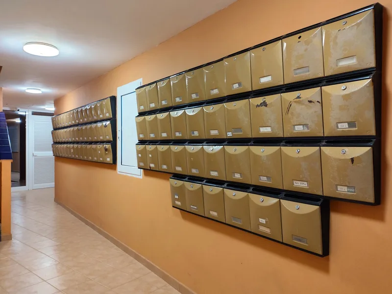 Rows of numbered metal mailboxes on an orange wall in an apartment building corridor